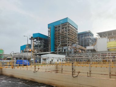 Zemin düzey bir perspektiften yakalanan resim, birbirine bağlı boru sistemleri ağına sahip büyük bir endüstriyel kompleks sergiliyor. Metal yapılarıyla karakterize edilen yapılar ve...