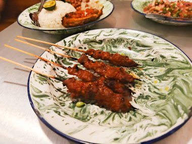 Restoran ortamında dekoratif bir tabakta servis edilen lezzetli satay şişler. Şişler mükemmelce kızartılmış ve aromatik baharatlarla tatlandırılmış, nefis bir karışım sunuyor.