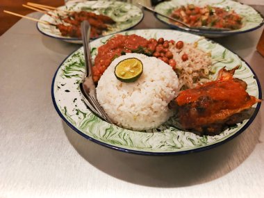 Nasi Campur 'un canlı bir tabağında Endonezya mutfağının zengin tatları, mis kokulu pirinç, baharatlı sambal ve lezzetli satay soslu leziz tavuk sergileniyor. Bu çeşitlilik ve...