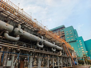 Sanayi sahnesinde, modern üretim ve üretim tesislerinin arkasındaki karmaşık mühendisliğin vurgulandığı karmaşık bir boru ve makine ağı sergileniyor. Görüntü, özünü yakalar.