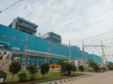 Bu görüntü, çarpıcı mavi cephesi ve bulutlu gökyüzünün altındaki yeşil alanları ile kömürle çalışan bir enerji santralini yakalıyor. Elektrik santrali endüstriyel enerji üretimini simgeliyor.