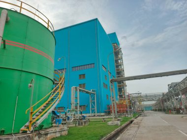 Bu görüntü enerji altyapısı ve depolama çözümlerinin canlı renklerde olduğu canlı bir endüstriyel kompleksi gösteriyor. Sahnede büyük bir yeşil depolama tankı, mavi bir endüstriyel bina ve