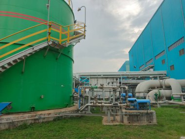 Bu resim, büyük tanklar, karmaşık boru sistemleri ve modern binalara odaklı bir endüstriyel kompleksi gösteriyor. Olay yeri, bir üretim veya depolama tesisinin altyapısını vurguluyor,