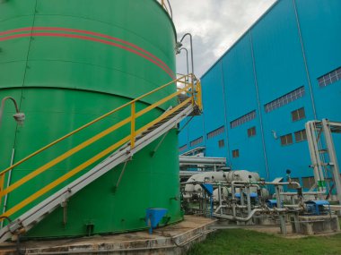 Bu resim, çarpıcı mavi endüstriyel bina kompleksinin yanında canlı yeşil bir depolama tankının yer aldığı endüstriyel bir manzarayı gösteriyor. Sahne görünür bir şekilde tamamlandı.