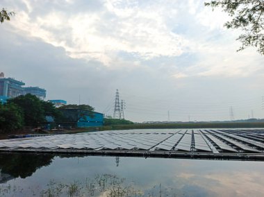 Sakin bir göl üzerinde yüzen bir güneş çiftliğinin bulunduğu sakin bir manzara, gökyüzünü ve çevreyi yansıtıyor. Güneş panellerinin sıraları su boyunca uzanıyor, yenilikçi kullanımını gösteriyor