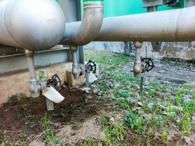 Bu görüntü, endüstriyel bir boru sisteminin bir kısmını bir dış fona göre ayarlanmış, önemli vanaları olan bir bölümünü yakalıyor. Metal borular ve mekanik bileşenler işlevsel bir altyapı olduğunu gösteriyor.,