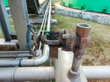 Bu, yağ ve gaz rafinerisinde çekilen yıpranmış dokuyla endüstriyel bir boru vanasının yakın çekimi. Görüntü kapakçığın karmaşık detaylarını gösteriyor, metali vurguluyor.