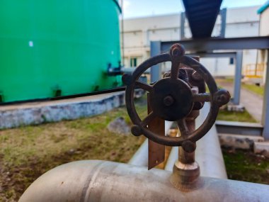 Açık hava üretim tesisinde endüstriyel bir boru hattı sisteminde kapakçık kontrolünü gösteren yakın plan bir çekim, karmaşık tasarım ve sağlam yapı kesinliği ve mühendisliği vurguluyor.