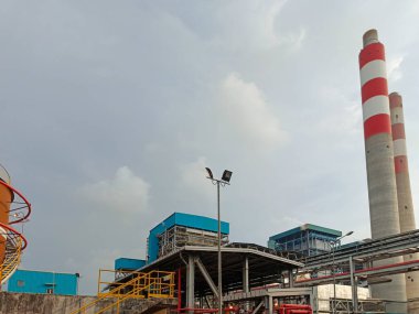 Bu görüntü bulutlu bir günde sanayi altyapısını ve bacalarını vurgulayan bir enerji santralini yakalıyor. Enerji üretimi için gerekli karmaşık mekanizmaları ve yapıları gösteriyor. Şey...