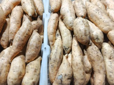 Bir süpermarketin üretim bölümünde sergilenen organik tatlı patateslerin bol miktarda sergilendiği yakın plan bir çekim. Görüntü, kökün ham, topraksı tonlarını ve dokularını vurgular.