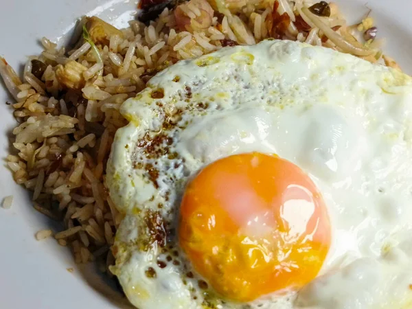 Görsel olarak cezbedici bir tabak kızarmış pilav mükemmel pişmiş, güneşli bir yumurta ile süslenir ve enfes bir mutfak deneyimi sunar. Yumurtanın altın sarısı ve kahverengi kenarları.