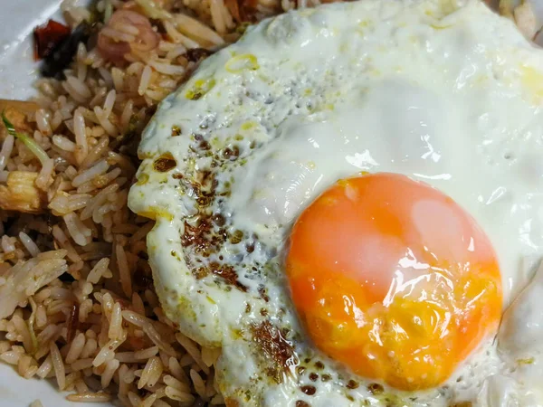 Bu resim, üzerinde mükemmel pişmiş, güneşte pişmiş yumurta olan bir tabak pilavın yakın çekim görüntüsünü içeriyor. Yemek lezzetli ve iştah açıcı görünüyor. Yumurta zengin ve kremalı.