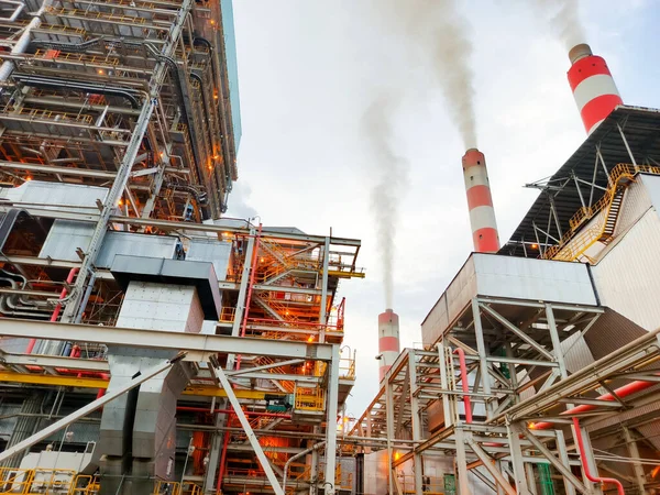 Bu görüntüde öne çıkan kırmızı ve beyaz çizgili bacaları olan endüstriyel bir enerji santrali görülüyor. Sahne endüstriyel yapının büyüklüğünü ve karmaşıklığını vurguluyor.