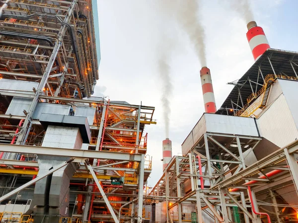 Bu görüntü, borular, yapılar ve bacalardan oluşan ağıyla bir enerji santrali yakalıyor duman salıyor, endüstriyi ve enerji üretimini sembolize ediyor, çevresel kaygıları vurguluyor ve