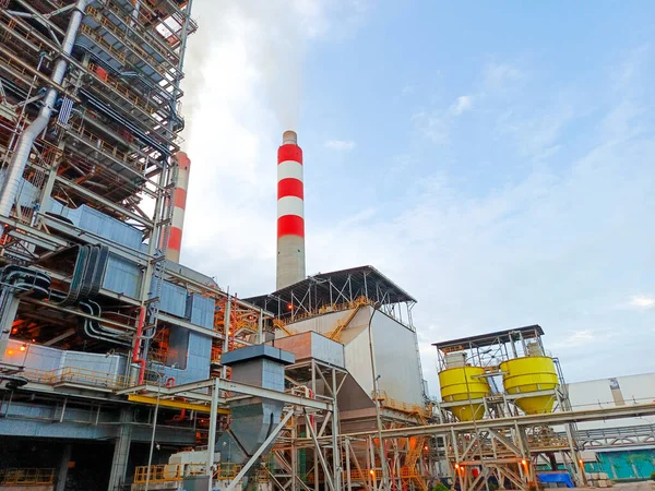 Düşük açılı bir çekimde geniş bir endüstriyel kompleks sergileniyor. Birden fazla bacası olan gökyüzü bulutlu. Görüntü bir enerji santralinin ölçeğini yakalıyor, karmaşık ağı vurguluyor