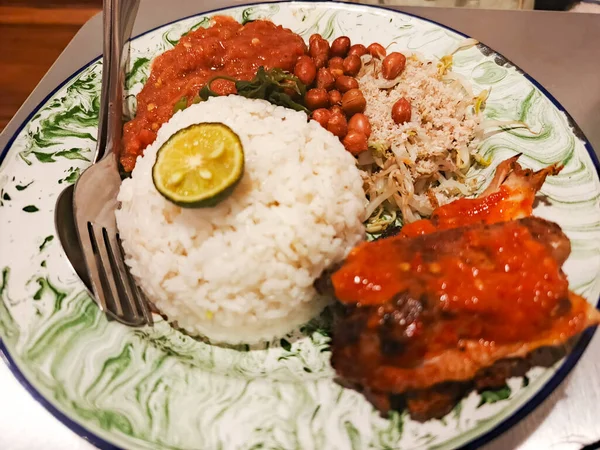 Geleneksel bir Endonezya yemeği olan Nasi Campur 'un canlı bir tabağında, beyaz pirinç harmonik bir karışım, bol soslu sulu tavuk ve çeşitli sebze parçaları sergileniyor. Mutfak lezzeti.