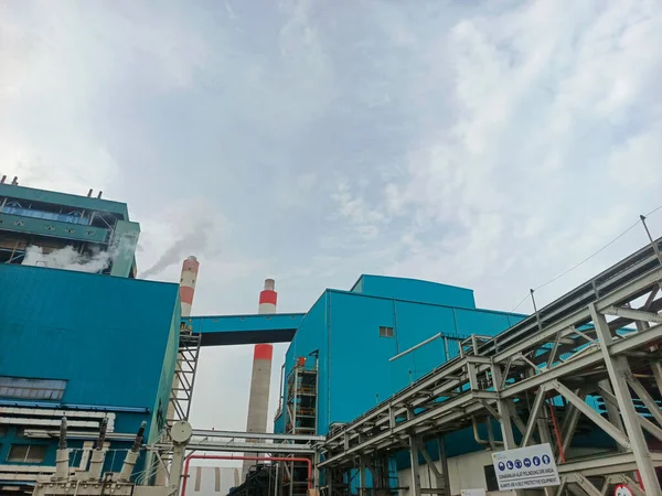 Bu görüntü, bulutlu bir gökyüzüne doğru yayılan duman yayan önde gelen bacaların yer aldığı endüstriyel bir kompleksi yakalıyor. Çelik yapılar ve binalar manzarayı oluşturarak enerji üretimini vurguluyor