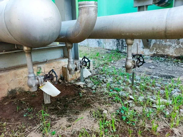 Bu görüntü, endüstriyel bir boru sisteminin bir kısmını bir dış fona göre ayarlanmış, önemli vanaları olan bir bölümünü yakalıyor. Metal borular ve mekanik bileşenler işlevsel bir altyapı olduğunu gösteriyor.,