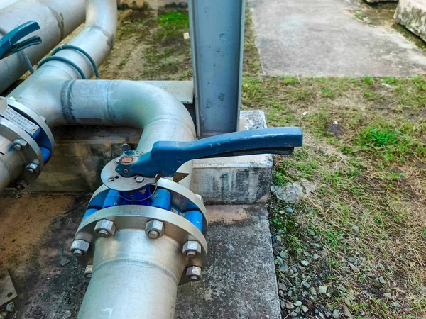 Yakın planda çekilen görüntülerde önde gelen bir kapakçık ve flanj bağlantısına sahip endüstriyel boru hattı sistemi sergileniyor. Metal borular ve beton destekleri bir arka fona dayanıyor. Bu sistem...