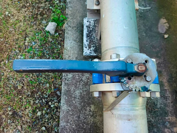 Mavi saplı metal bir endüstriyel boru hattını gösteren yakın çekim, işlevselliğini ve karmaşık yapısını vurguluyor. Vana boru hattına cıvata ve fındıkla bağlı.,