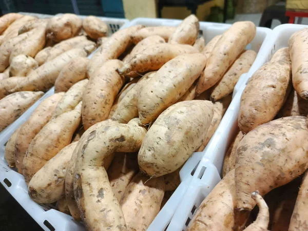 Yakın plan çekimde, beyaz plastik bir kabın içindeki taze, çiğ yer elması yığını görülüyor. Yer elmaları bir markette sergileniyor, satın alınmaya hazır. Görüntü, doğal dokuyu vurgular ve...