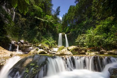 Serin doğal manzara, yoğun yeşil orman yaprakları arasında, yosun kaplı kayaların üzerinden akan birkaç şelaleye ev sahipliği yapar, barışçıl ve canlı bir açık hava ortamı yaratır.