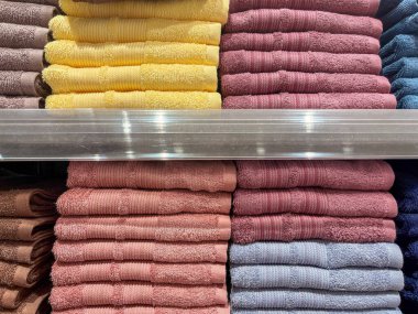 Yumuşak renkli pamuk havlular canlı sarı kestane rengi kahverengi ve mavi renkler içeren bir perakende rafında düzenli olarak düzenlenir.