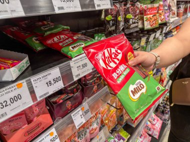 Parlak bir süpermarket koridorunda alışveriş yaparken elinde çikolatalı gofret paketi olan kişi çeşitli paket yiyecek ve atıştırmalıklarla dolu.