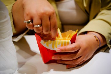 Bir insanın elleri, özel kırmızı ve beyaz bir kartondan altın patates kızartması kapar ve popüler bir atıştırmalığı ön plana çıkarır..