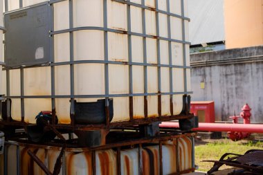 Endüstriyel orta büyüklükteki konteynırlar açık havada toplanmış metal kafeslerinde belirgin pas var ve imalat ortamında ağır kullanım belirtileri gösteriyor.