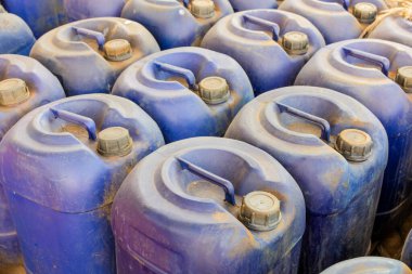 Fıçı Mavi plastik kaplar, sıvı kimyasalları depolamak ve atık maddeleri yönetmek için kullanılan çok sayıda endüstriyel kutunun sergilendiği bir depoda yakın bir şekilde bir araya toplanır.