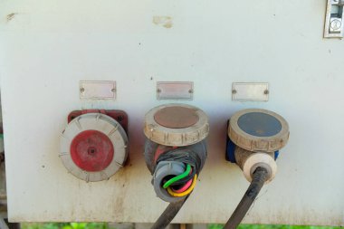 Yıpranmış bir panelde, kablolar ve konnektörlerle üç endüstriyel elektrik prizine yakın çekim. Açık hava güç kaynağı kavramı.