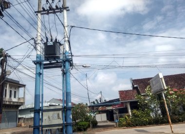 Jambi, Endonezya. 29 Aralık 2025. İki mavi yüksek voltajlı elektrik direği, arka planda konut evleri ve temiz bir gökyüzü var..