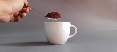 Kaşıkla bardağa kahve tozu döken bir el. Günlük rutin, içecek hazırlama ve kafein konsepti