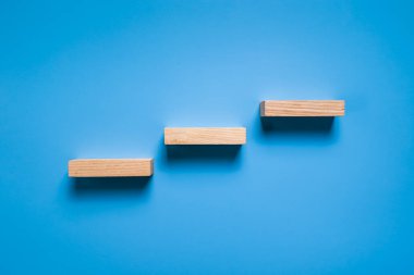 Üç tahta blok mavi arkaplanda izole merdiven formu oluşturuyor.