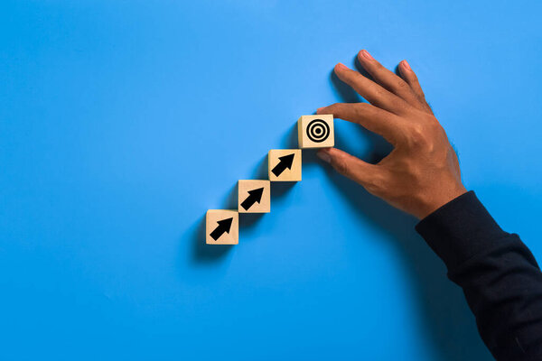 male hand put arrow up and target on wooden blocks isolated on blue background. concept of goals achievement