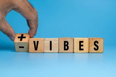 Erkek eli, mavi arka planda pozitif ve negatif titreşimli tahta blokları çevirir.