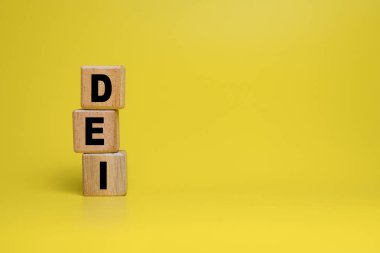 DEI ya da çeşitlilik özsermayesi ve kapsayıcı kelimeler sarı arka planda izole edilmiş tahta bloklar üzerinde sembolize edilir. Boşluğu kopyala