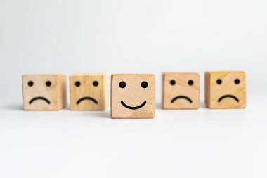 Üzgün yüzler ve gülen yüz ifadeleri ahşap bloktaki beyaz arka planda izole edilmiş ifade.