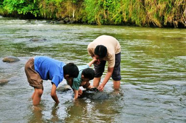 Bir baba, çocuklarına nehir kıyısındaki kayaları ve sığ suları keşfederken yardım eder..