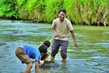 Bir baba, çocuklarına nehir kıyısındaki kayaları ve sığ suları keşfederken yardım eder..