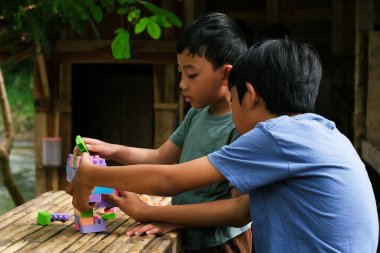 İki çocuk renkli bloklar inşa etmek için birlikte çalışıyor, doğal ortamlarda eğlenceli ve yaratıcı bir etkinliğin tadını çıkarıyorlar..