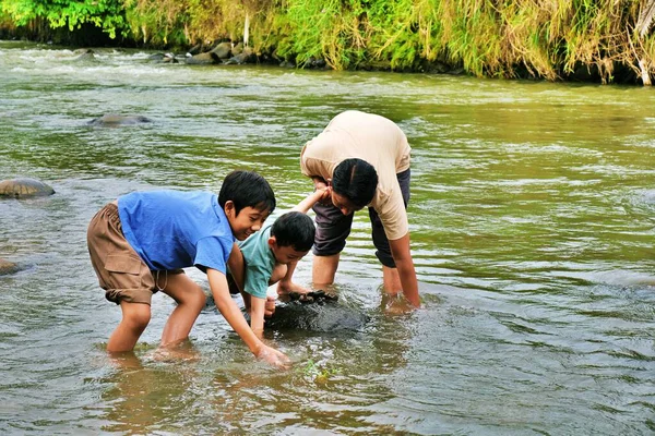 Bir baba, çocuklarına nehir kıyısındaki kayaları ve sığ suları keşfederken yardım eder..