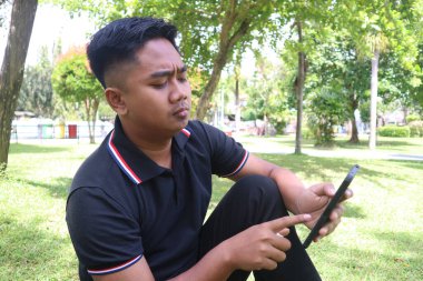 Parkta telefonunu kullanarak odaklanmış ve ciddi bir yüz ifadesi olan genç bir adam..