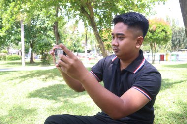Genç bir adam parkta telefonuyla fotoğraf çekiyor..