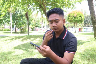 Parkta telefonunu kullanırken ciddi ve düşünceli bir ifade takınan genç bir adam..