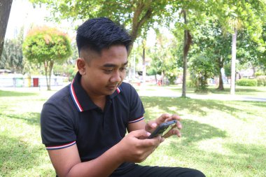 Genç adam parkta telefonuyla kayıyor. Teknoloji, eğlence ve günlük yaşam tarzı..