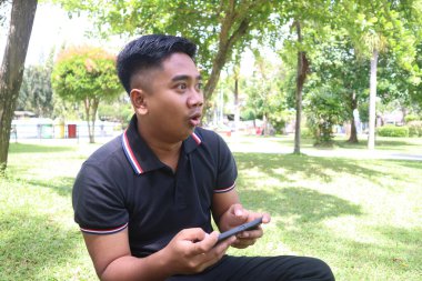 Parkta telefonundan başka yöne bakan şaşırmış bir yüzü olan genç adam..