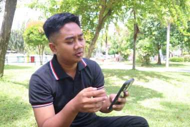 Parkta telefonla konuşan ya da şarkı söyleyen genç bir adam. İfade, teknoloji ve günlük yaşam tarzı.