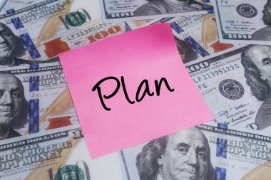 ABD doları banknotları üzerine, mali planlama, yatırım stratejileri, tasarruf hedefleri ve ticari başarı kavramlarını gösteren pembe Plan yapışkan bir nota yakın plan